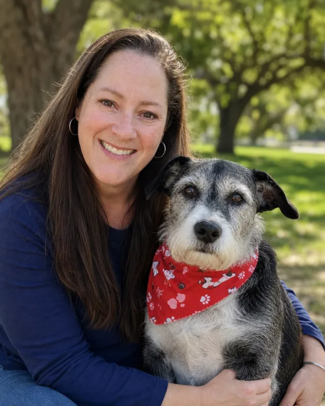 Kristen smiling outdoors with a senior black-and-white dog.