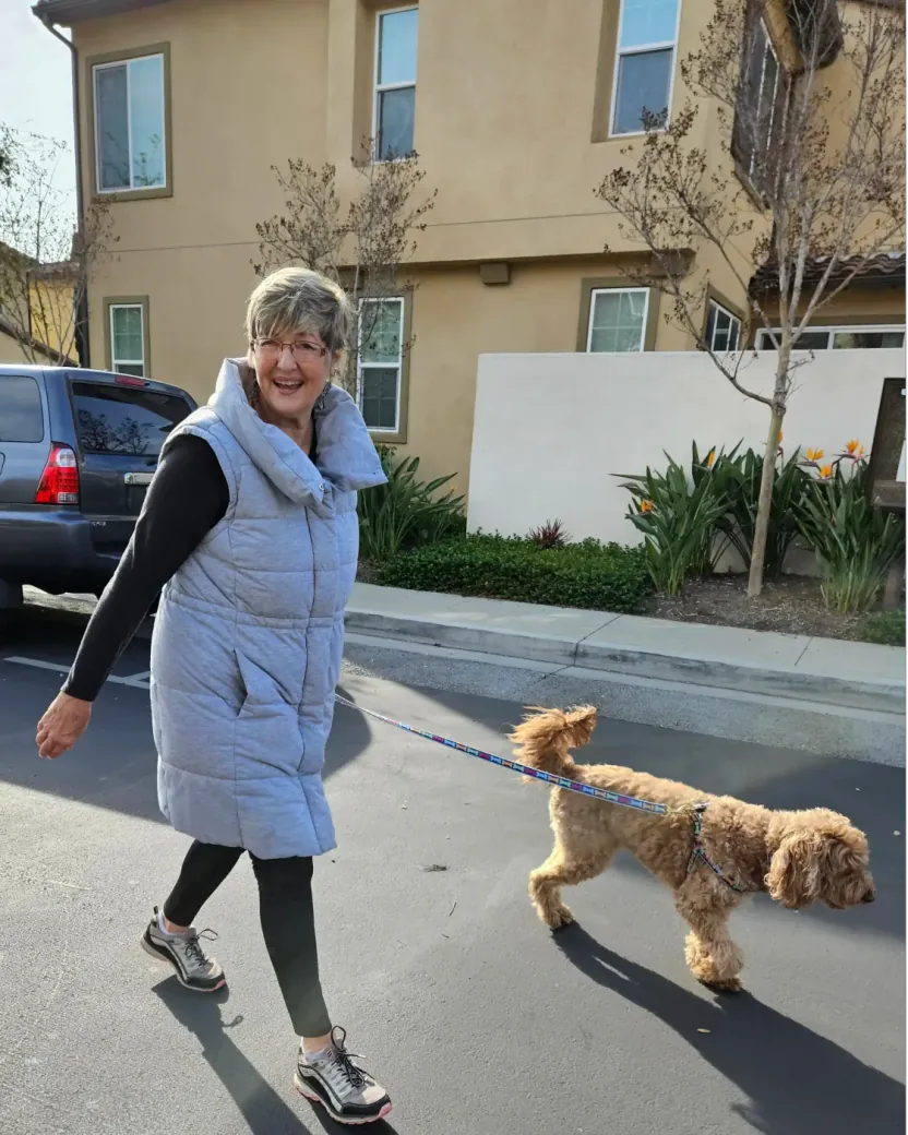 Teresa smiling while walking a small apricot doodle on a neighborhood street.